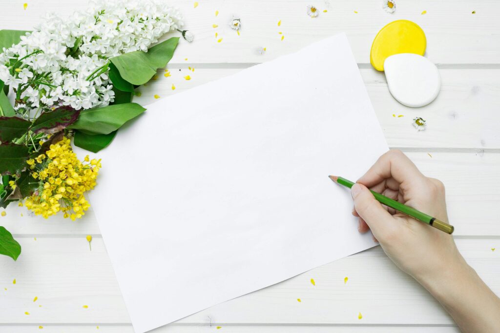 person writing on a page next to flowers
