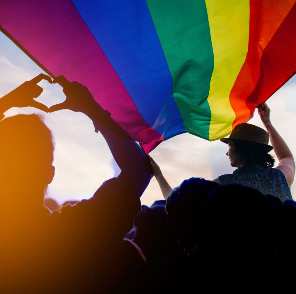 person holding a pride flag while another makes a heart with their hands